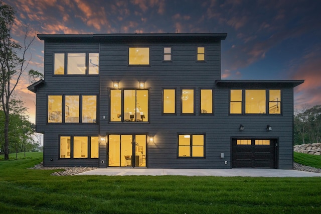 back house at dusk with a garage and a lawn