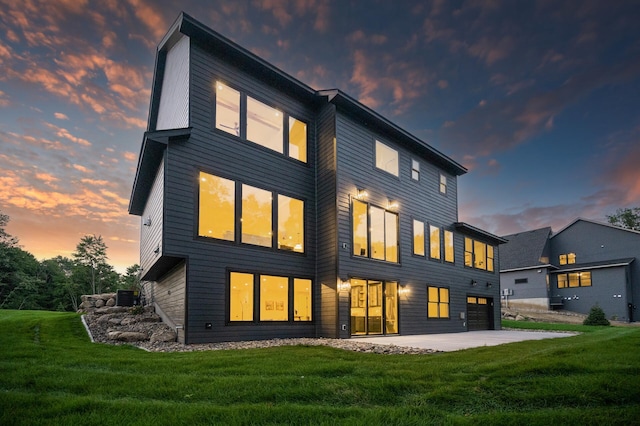 back house at dusk with central AC unit, a lawn, and a patio