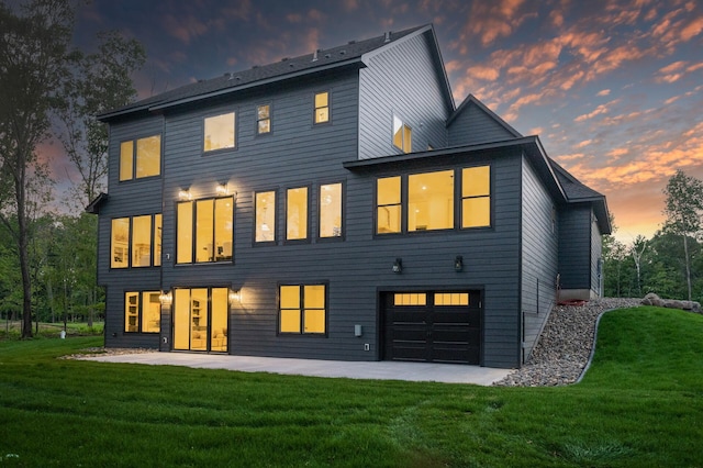 back house at dusk with a garage, a yard, and a patio area