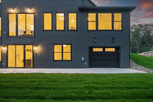 back house at dusk with a garage and a yard