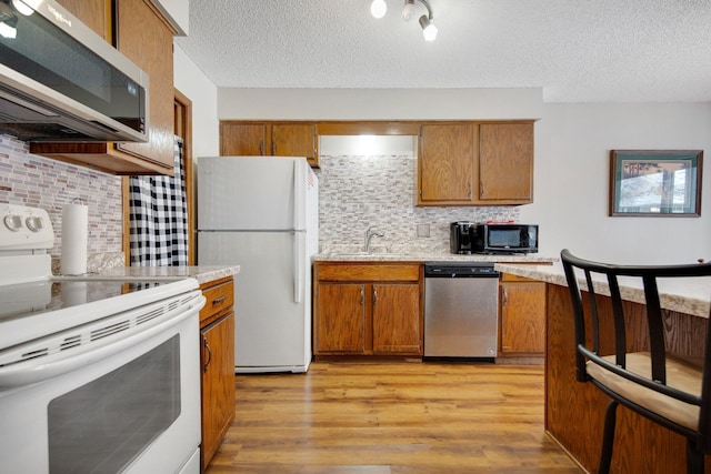 kitchen with appliances with stainless steel finishes, sink, light hardwood / wood-style floors, and a textured ceiling