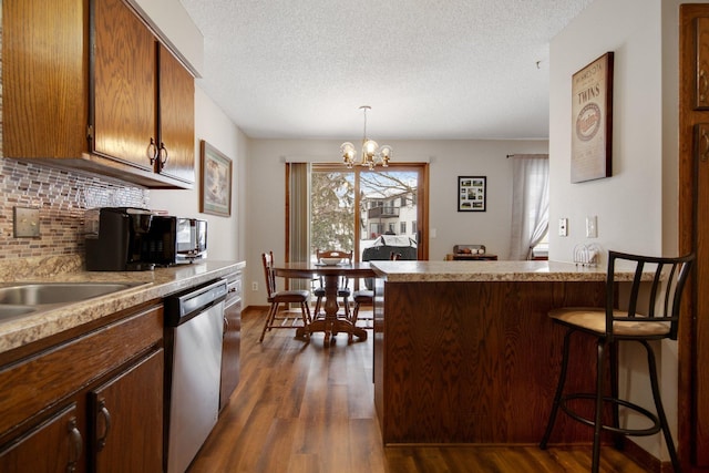 kitchen featuring dark wood-type flooring, a textured ceiling, stainless steel dishwasher, pendant lighting, and decorative backsplash