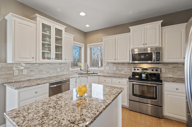 kitchen featuring light wood-style flooring, glass insert cabinets, appliances with stainless steel finishes, white cabinetry, and a sink