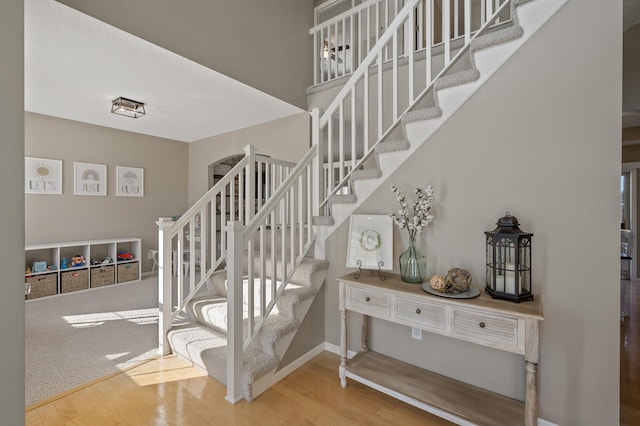 stairway with a high ceiling, wood finished floors, and baseboards