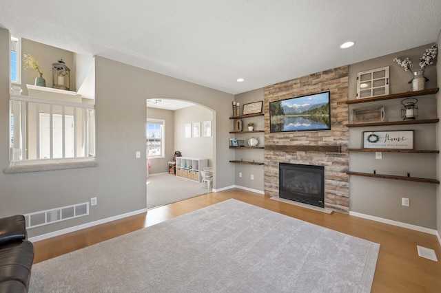 living area featuring arched walkways, visible vents, a fireplace, and wood finished floors