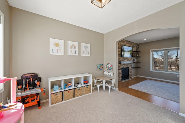 game room featuring a stone fireplace, carpet, wood finished floors, and baseboards