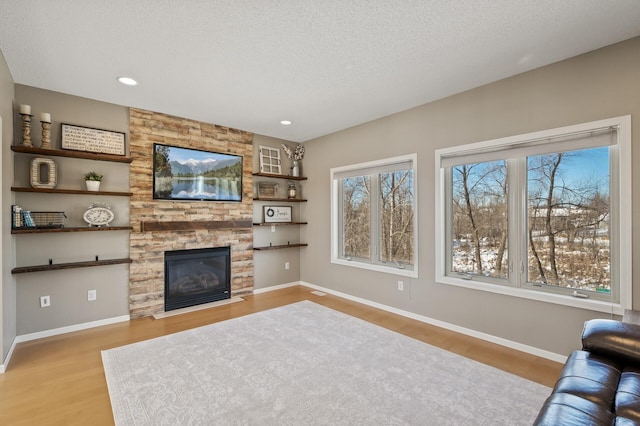 living area with a textured ceiling, recessed lighting, a fireplace, baseboards, and light wood finished floors