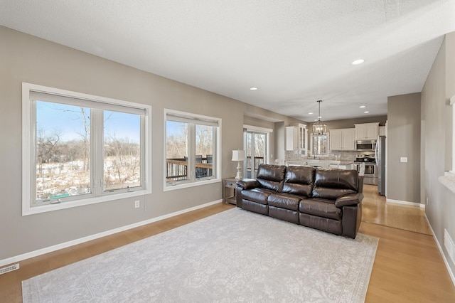 living room with light wood-style flooring, visible vents, baseboards, and recessed lighting