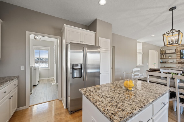 kitchen with arched walkways, light wood-style floors, white cabinets, stainless steel fridge with ice dispenser, and light stone countertops