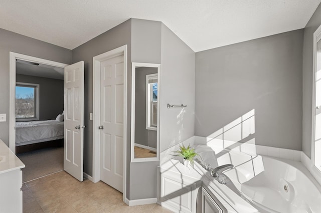 ensuite bathroom with ensuite bathroom, a textured ceiling, tile patterned flooring, a whirlpool tub, and baseboards