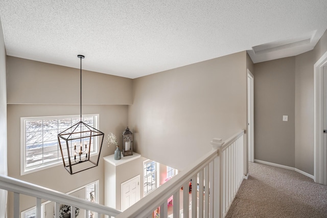 corridor with baseboards, carpet floors, a textured ceiling, and a notable chandelier