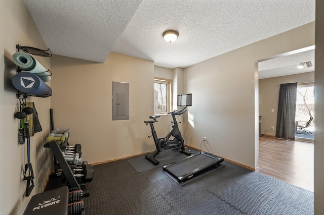 workout area featuring a textured ceiling, electric panel, and baseboards