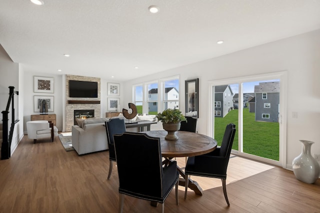 dining room featuring hardwood / wood-style flooring, a stone fireplace, and a textured ceiling