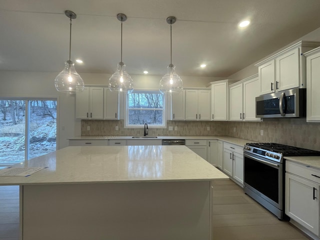 kitchen with appliances with stainless steel finishes, pendant lighting, sink, white cabinets, and a center island