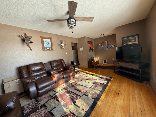 living room featuring wood-type flooring, ceiling fan, and a textured ceiling