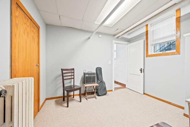 living area featuring a drop ceiling, baseboards, radiator heating unit, and carpet