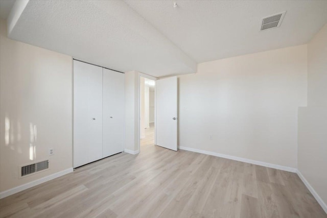 unfurnished bedroom featuring light hardwood / wood-style floors, a closet, and a textured ceiling