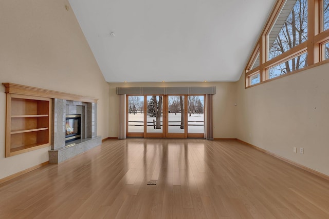 unfurnished living room with a high end fireplace, high vaulted ceiling, and light wood-type flooring