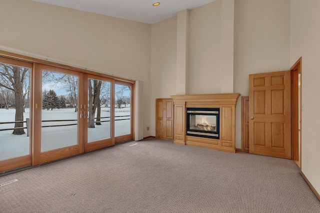 unfurnished living room with light carpet, french doors, a high ceiling, and a multi sided fireplace