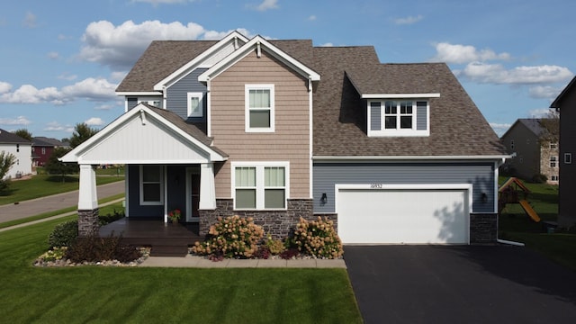 craftsman house with driveway, a shingled roof, a front yard, and stone siding