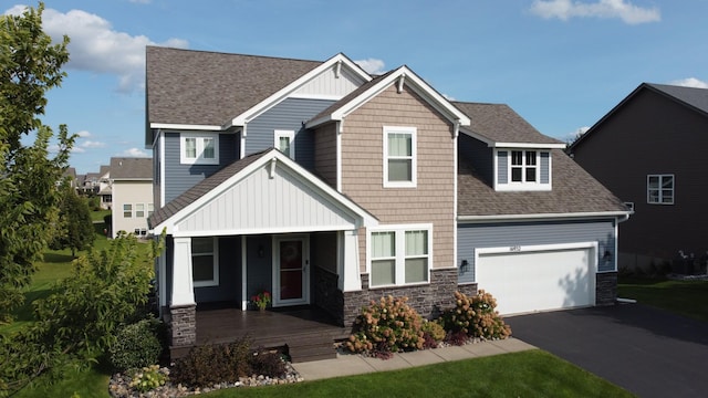 craftsman-style house with aphalt driveway, an attached garage, covered porch, stone siding, and roof with shingles