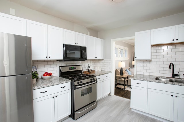 kitchen with light stone counters, stainless steel appliances, sink, and white cabinets