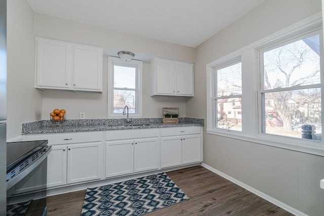 kitchen with stainless steel electric range oven, sink, white cabinets, light stone countertops, and dark wood-type flooring