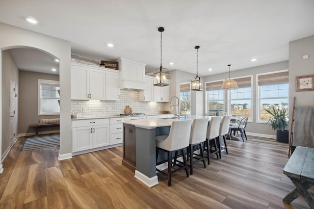 kitchen with hardwood / wood-style floors, decorative backsplash, white cabinets, a center island with sink, and decorative light fixtures