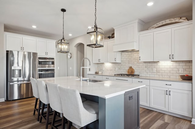 kitchen with appliances with stainless steel finishes, pendant lighting, sink, white cabinets, and a center island with sink