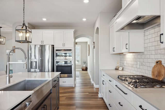 kitchen featuring sink, custom exhaust hood, hanging light fixtures, appliances with stainless steel finishes, and white cabinets