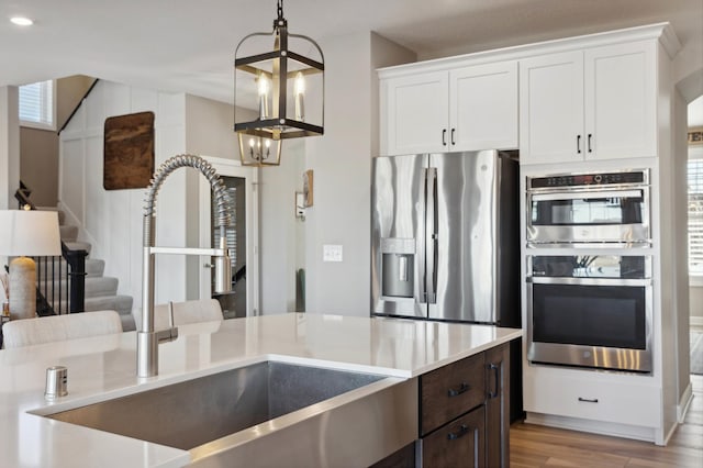 kitchen featuring white cabinetry, appliances with stainless steel finishes, decorative light fixtures, and sink