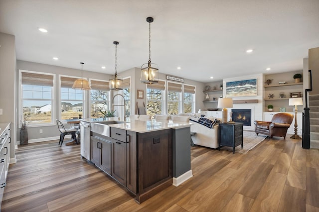 kitchen featuring hardwood / wood-style floors, decorative light fixtures, an island with sink, sink, and dark brown cabinets