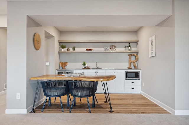 bar with white cabinetry, stainless steel microwave, sink, and light hardwood / wood-style flooring