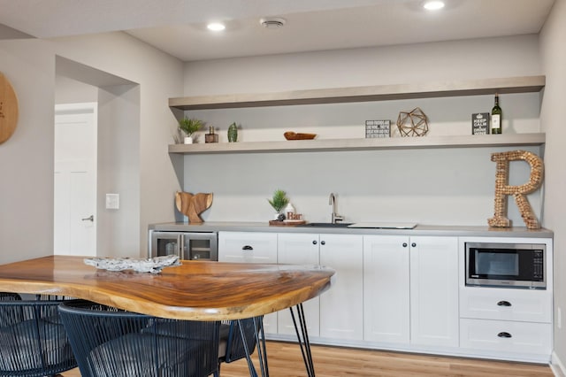 bar featuring stainless steel microwave, butcher block countertops, white cabinetry, wine cooler, and light hardwood / wood-style flooring