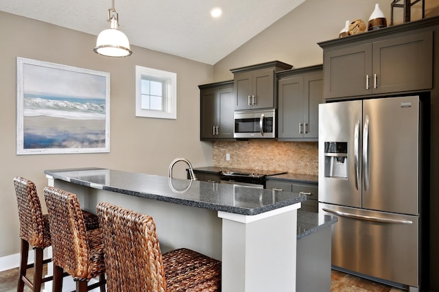 kitchen with appliances with stainless steel finishes, a breakfast bar, lofted ceiling, dark stone counters, and a center island with sink