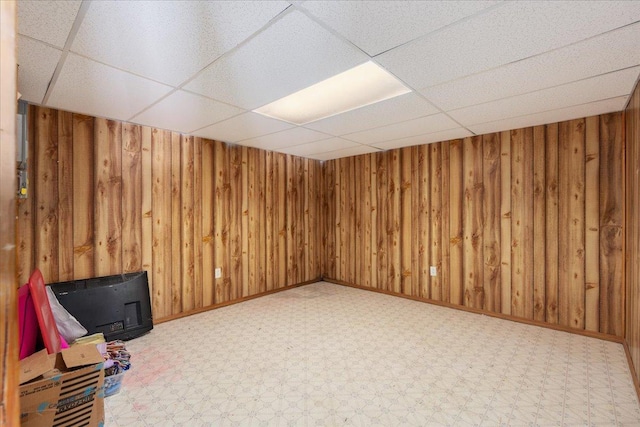 basement featuring a paneled ceiling and wood walls