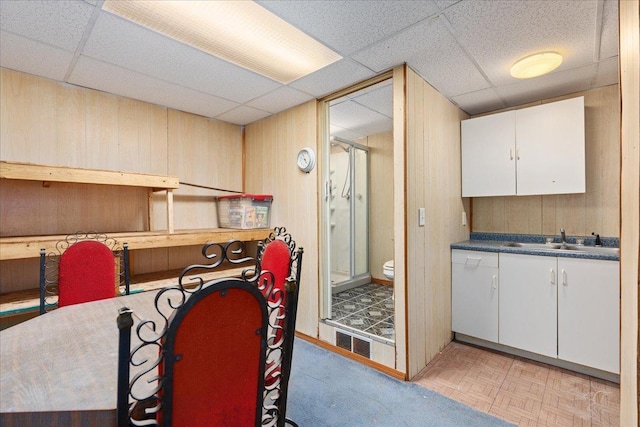 kitchen with white cabinetry, sink, a drop ceiling, and wooden walls