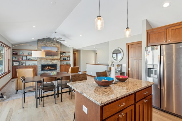 kitchen with vaulted ceiling, a kitchen island, a stone fireplace, pendant lighting, and stainless steel refrigerator with ice dispenser