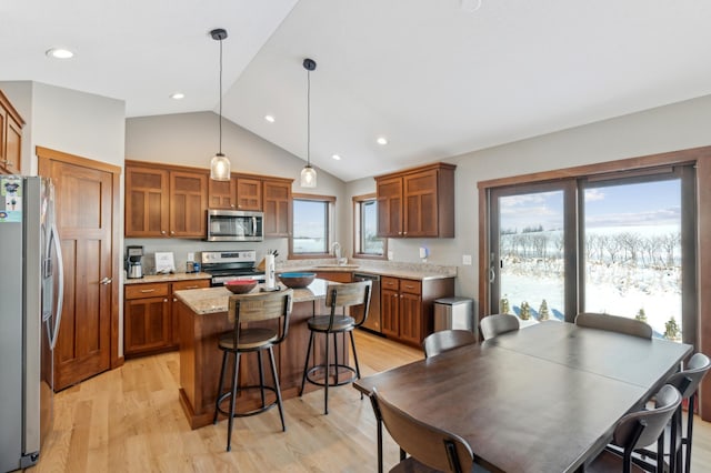 kitchen with light hardwood / wood-style flooring, appliances with stainless steel finishes, light stone countertops, a kitchen island, and decorative light fixtures