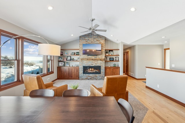 dining space featuring a stone fireplace, lofted ceiling, light hardwood / wood-style flooring, ceiling fan, and built in shelves