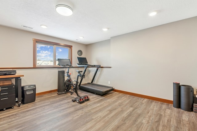 exercise room with a textured ceiling and light wood-type flooring