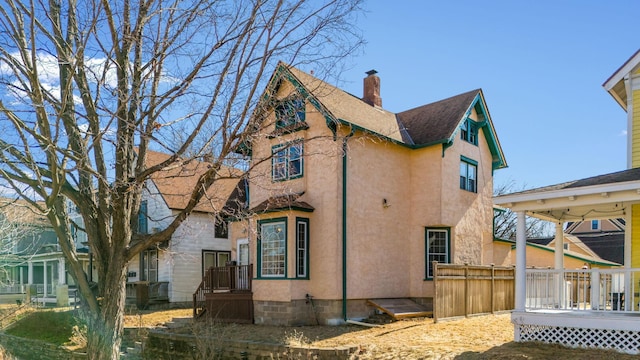 view of side of home featuring a shingled roof, a chimney, fence, and stucco siding