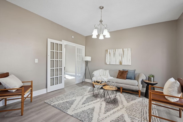 living area featuring baseboards, a chandelier, wood finished floors, and french doors