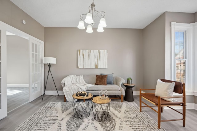 living room with a notable chandelier, baseboards, wood finished floors, and french doors