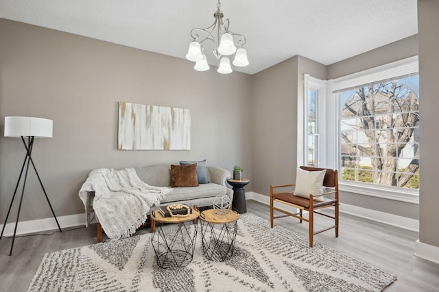 living area featuring an inviting chandelier, a textured ceiling, baseboards, and wood finished floors