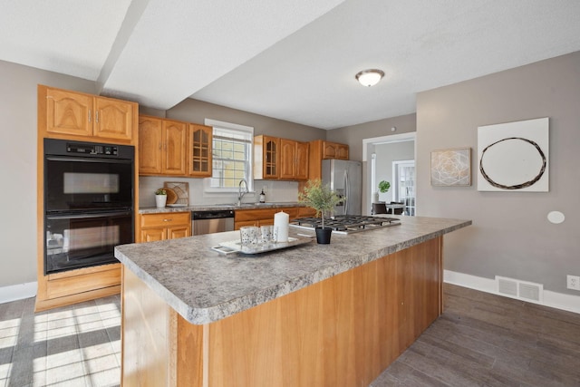 kitchen with a center island, visible vents, appliances with stainless steel finishes, glass insert cabinets, and baseboards