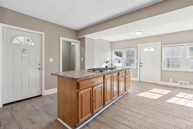 kitchen with brown cabinetry, a kitchen island, visible vents, and light wood-style floors