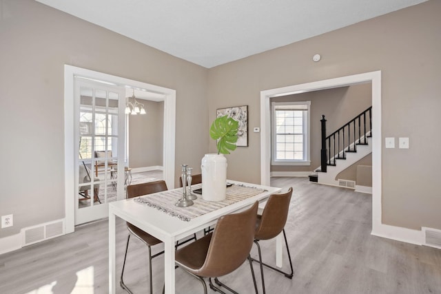 dining area featuring light wood-type flooring, visible vents, an inviting chandelier, and stairs