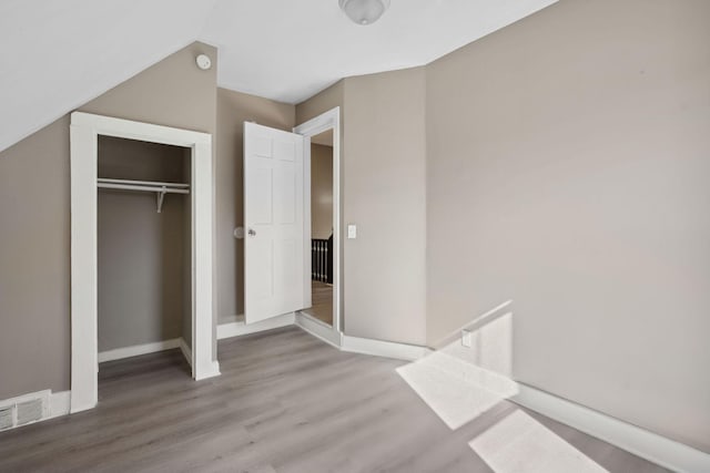 unfurnished bedroom with a closet, wood finished floors, visible vents, and baseboards