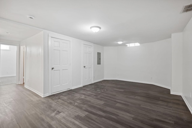 finished basement with baseboards, electric panel, visible vents, and dark wood-style flooring